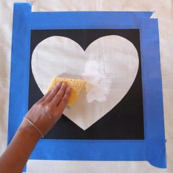 Sponge painting inside the heart stencil that is taped to the pillow cover.