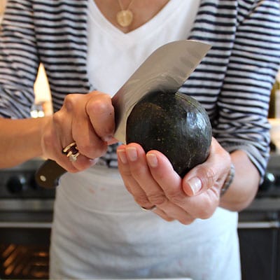 Woman cutting an avocado in half using a chef knife.