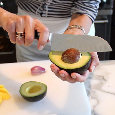 A woman punctures the seed of an avocado using a chef knife.