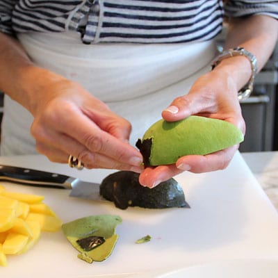 Woman removing the skin from a quarter piece of an avocado.