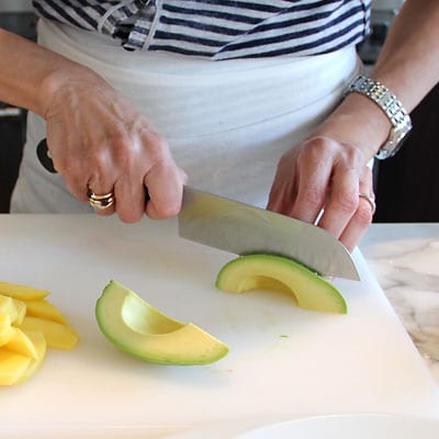 Avocado being cut into slices with a chef knife.